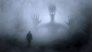 Uomo di spalle in un bosco avvolto dalla nebbia fitta. Sullo sfondo si intravvede una figura gigantesca di un alieno