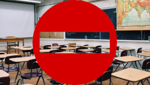 Un'aula scolastica completamente vuota. Sovrapposto, un cartello di divieto d'accesso
