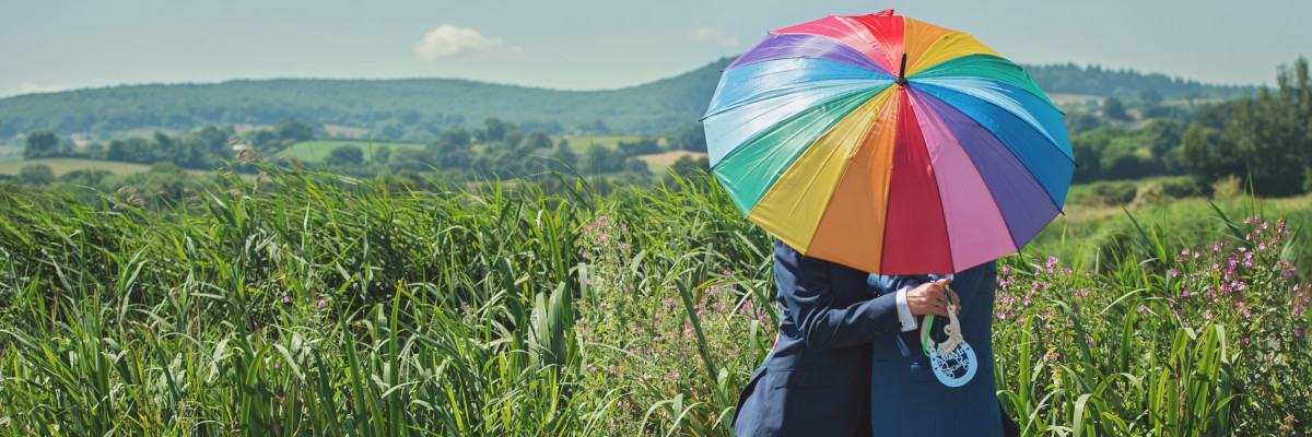 Due uomini si abbracciano, nascosti da un ombrello arcobaleno