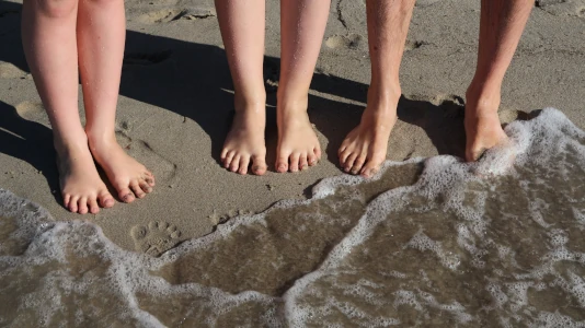 Sul bagnasciuga, i piedi nudi di donna, uomo e bambino. Da soli, con gli amici o con la famiglia, le vacanze in un campo di nudisti possono essere un vero punto di svolta per vincere la propria difficoltà a farsi vedere